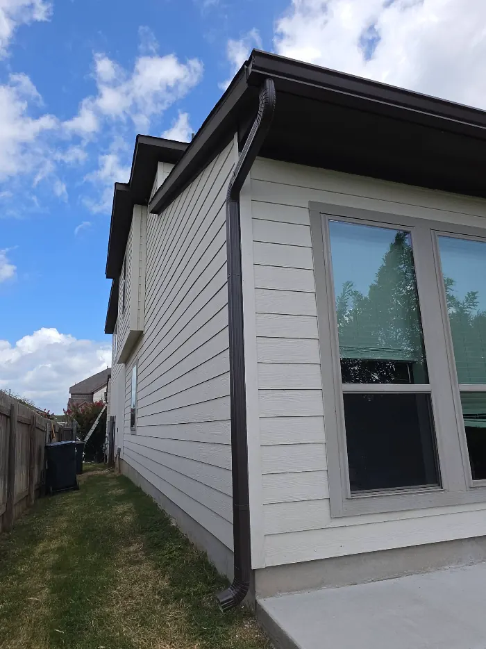Bronze seamless gutter and downspout running down a light-sided home